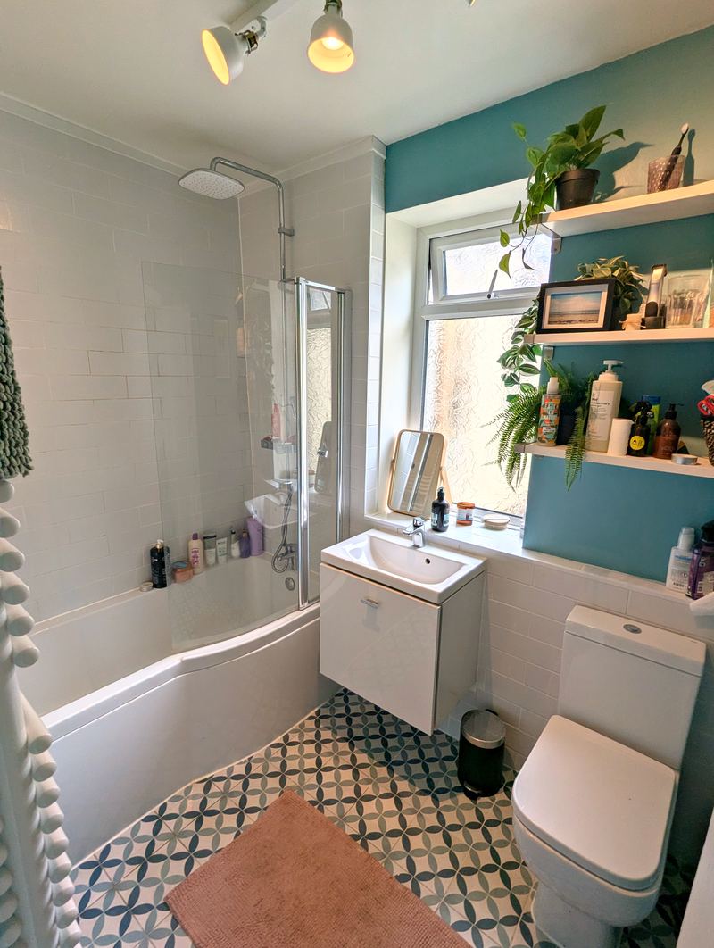 Bathroom with a bath and shower screen, basin, patterned floor tiles and open shelving