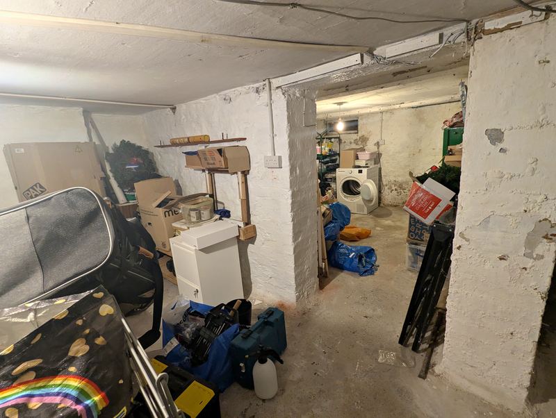 Whitewashed cellar room used for storage, with a washing machine