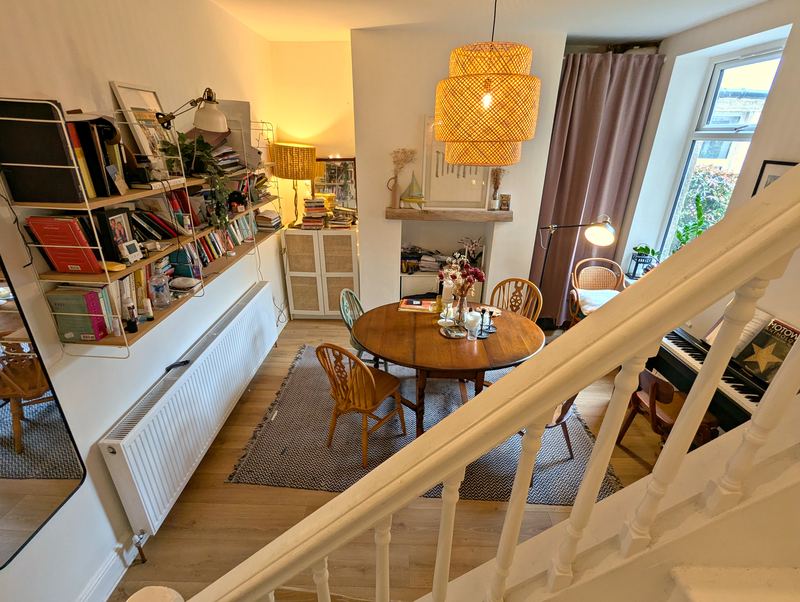 Dining room seen from the stairs, with a round table, fireplace, bookshelves and a piano
