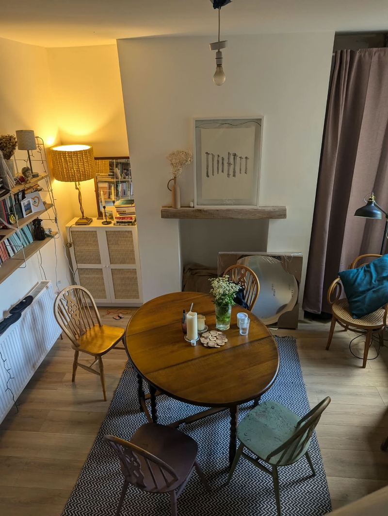 Dining room with a round table and chairs, a fireplace with a timber mantel and alcove shelving
