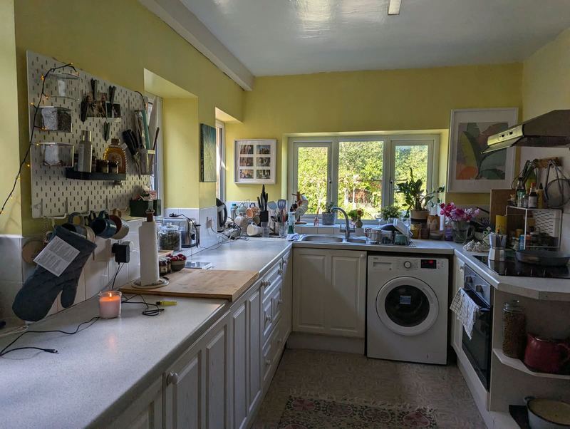 Galley kitchen with white units, yellow walls and a window over the sink looking onto the garden