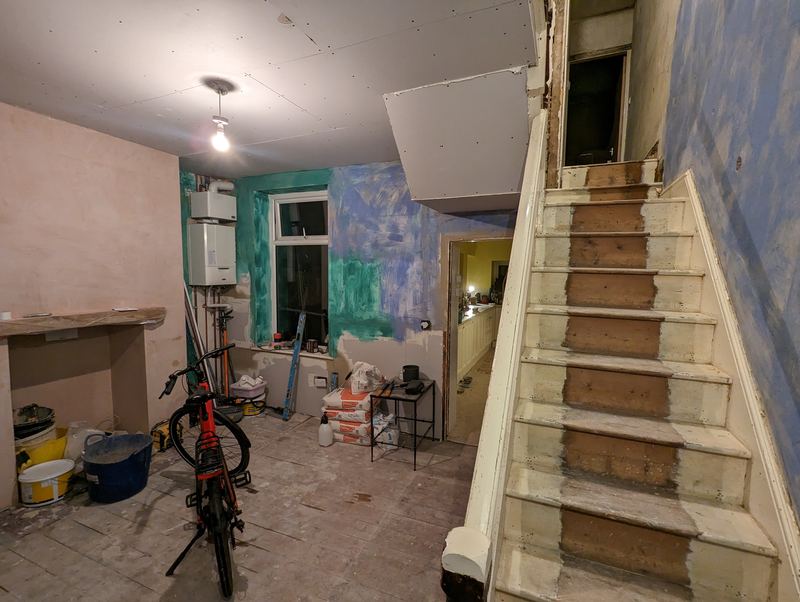 The downstairs rooms mid-renovation, with bare stairs and stripped walls